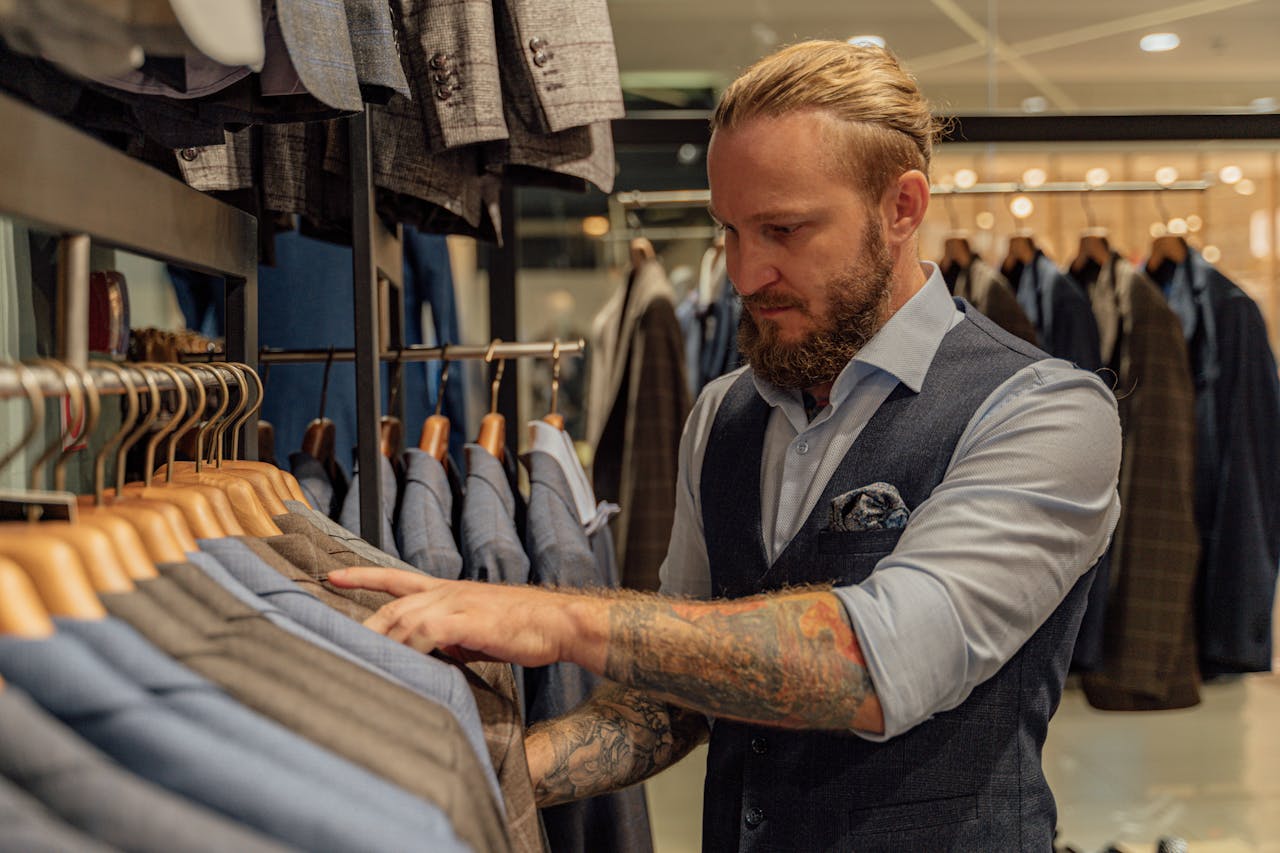 about-me-img Tattooed man selecting suits in a fashionable clothing store, elegant setting.